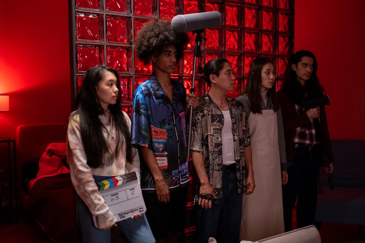 A diverse group of young filmmakers standing indoors with movie equipment, under red lighting.