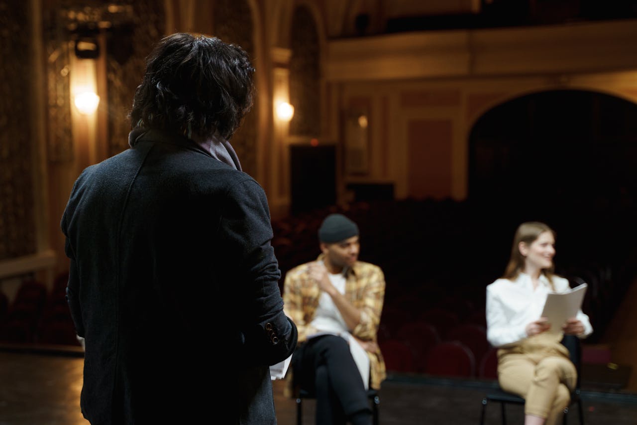 Actors rehearse on a classical theater stage with scripts before performance.